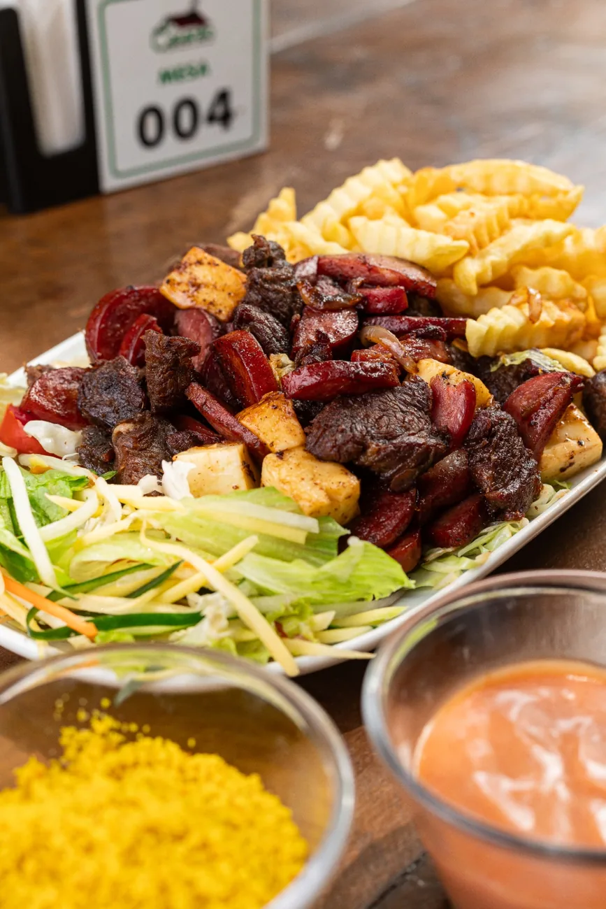 Prato misto de churrasco com carnes, batata frita, salada e farofa
